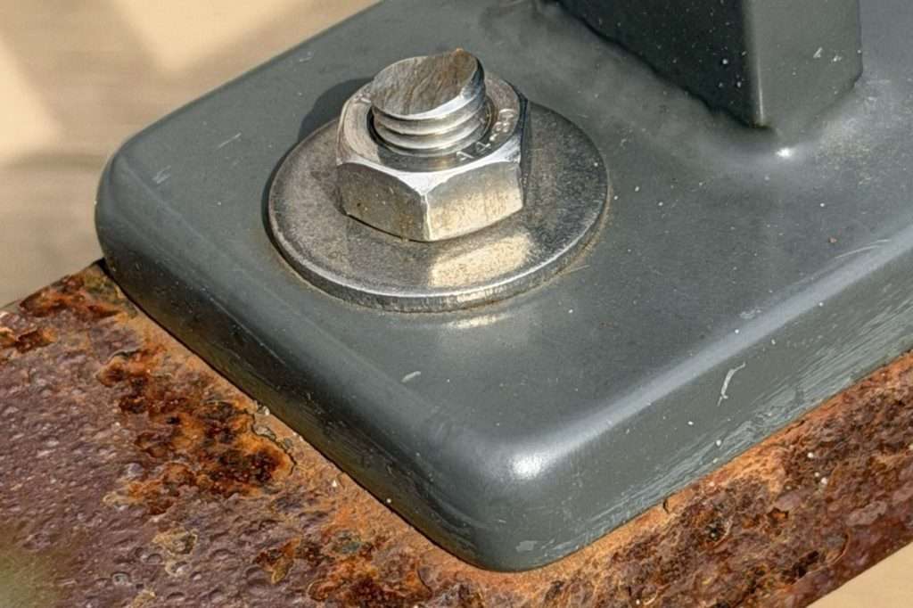 Rostender Unterholm eines Zauns unter einer beschichteten Fußplatte mit Edelstahlschraube